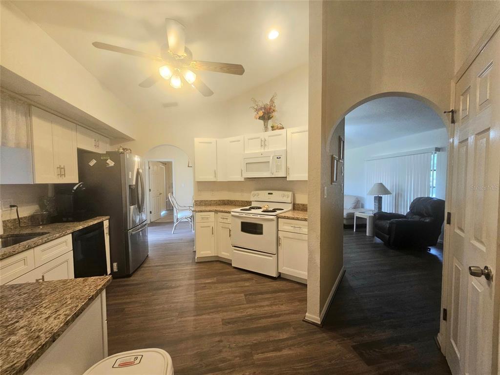 A kitchen with white cabinets, granite countertops, and stainless steel appliances opens into a living area — 1011 TROPICAL AVENUE NW, PORT CHARLOTTE, FL
