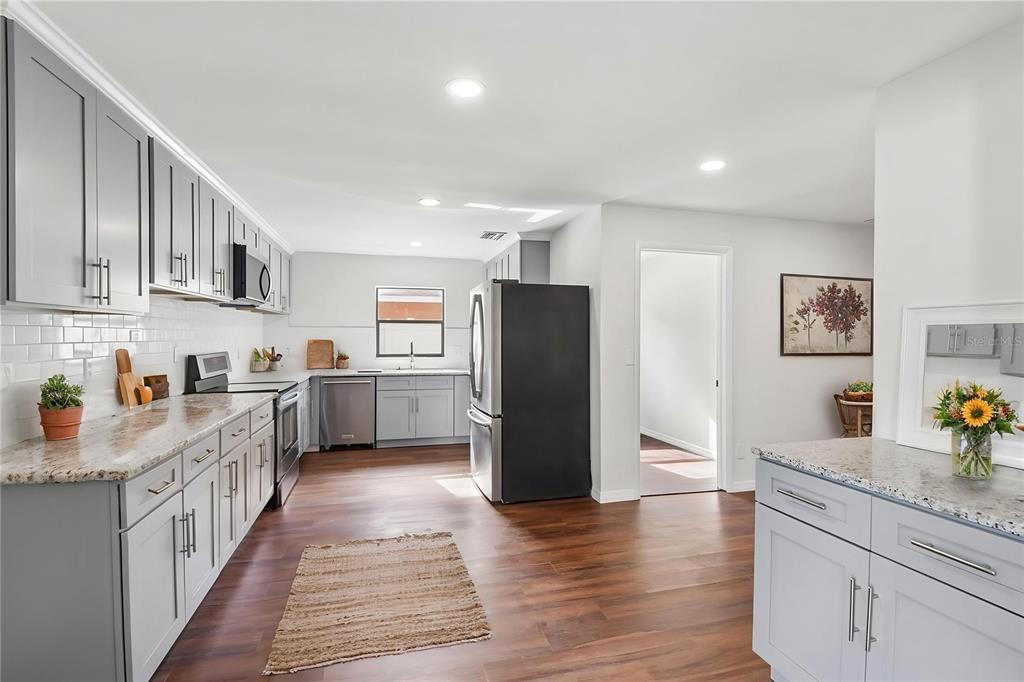 A kitchen features gray cabinets, granite countertops, stainless steel appliances, and dark wood flooring — 4545 DEBBIE LANE, LUTZ, FL