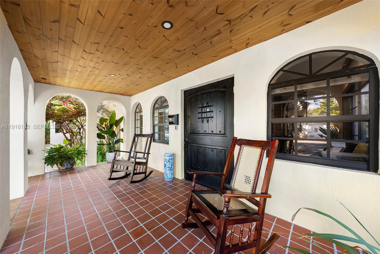A covered porch features a wood-paneled ceiling, terracotta tile flooring, and two wooden rocking chairs — 1650 SW 16th St, Miami FL 33145, MIAMI, FL