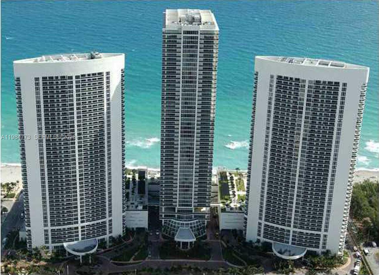 An aerial view shows three tall residential towers situated along a sandy beach and ocean — 1800 S Ocean Dr # 1606, Hallandale Beach FL 33009, HALLANDALE BEACH, FL