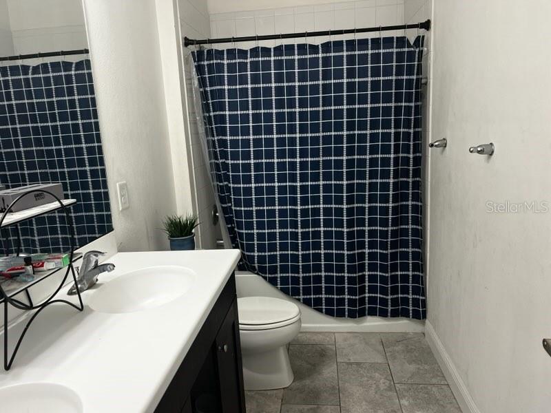 A bathroom features a white vanity, a toilet, and a blue grid-patterned shower curtain — 3516 WOODMONT DRIVE, PARRISH, FL