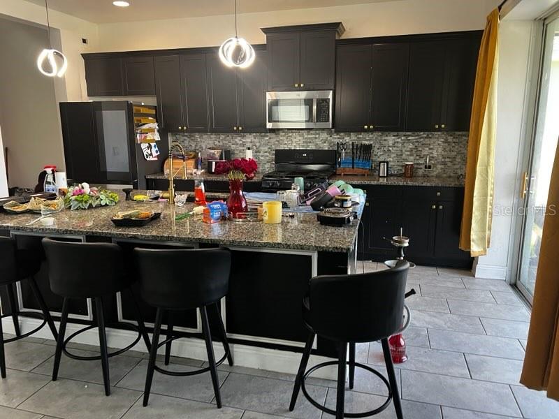 A kitchen features dark cabinetry, granite countertops, a tiled backsplash, and a large center island — 3516 WOODMONT DRIVE, PARRISH, FL
