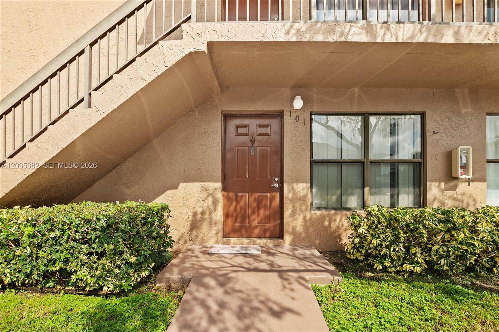 An exterior view of a ground-floor apartment entrance with a brown door and stairs — 10053 Winding Lake Rd # 101, Sunrise FL 33351, SUNRISE, FL