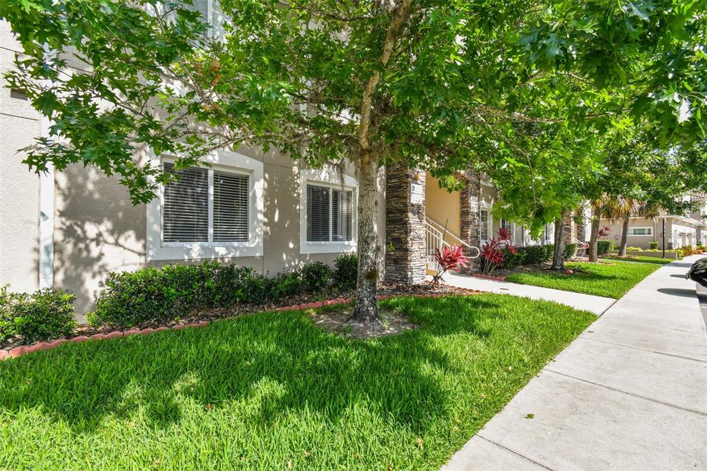 A multi-story apartment building exterior with a green lawn, sidewalk, and mature trees — 1231 GODAVARI WAY UNIT 103, WESLEY CHAPEL, FL