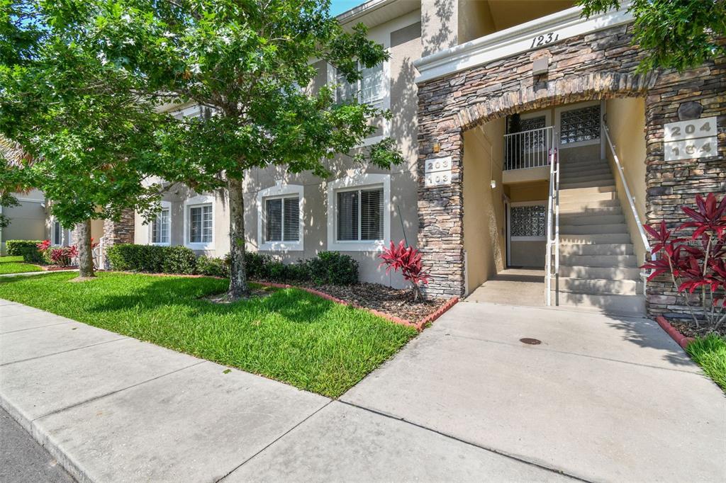 An exterior view of a multi-story apartment building with stone accents and a concrete staircase — 1231 GODAVARI WAY UNIT 103, WESLEY CHAPEL, FL