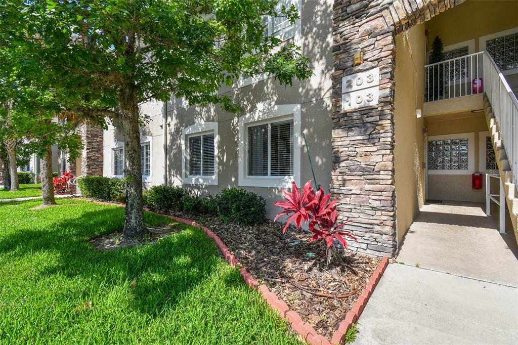 Exterior view of a multi-story apartment building with stone accents and a concrete walkway — 1231 GODAVARI WAY UNIT 103, WESLEY CHAPEL, FL