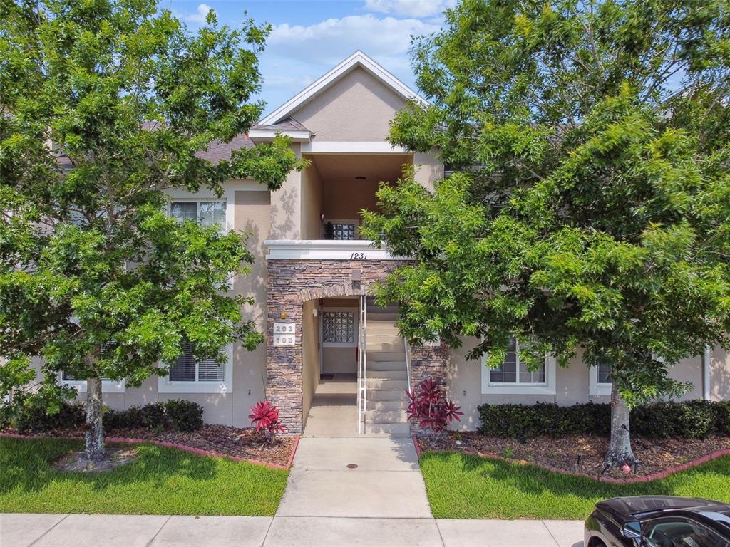 A two-story apartment building exterior features stone accents, a central staircase, and surrounding trees — 1231 GODAVARI WAY UNIT 103, WESLEY CHAPEL, FL