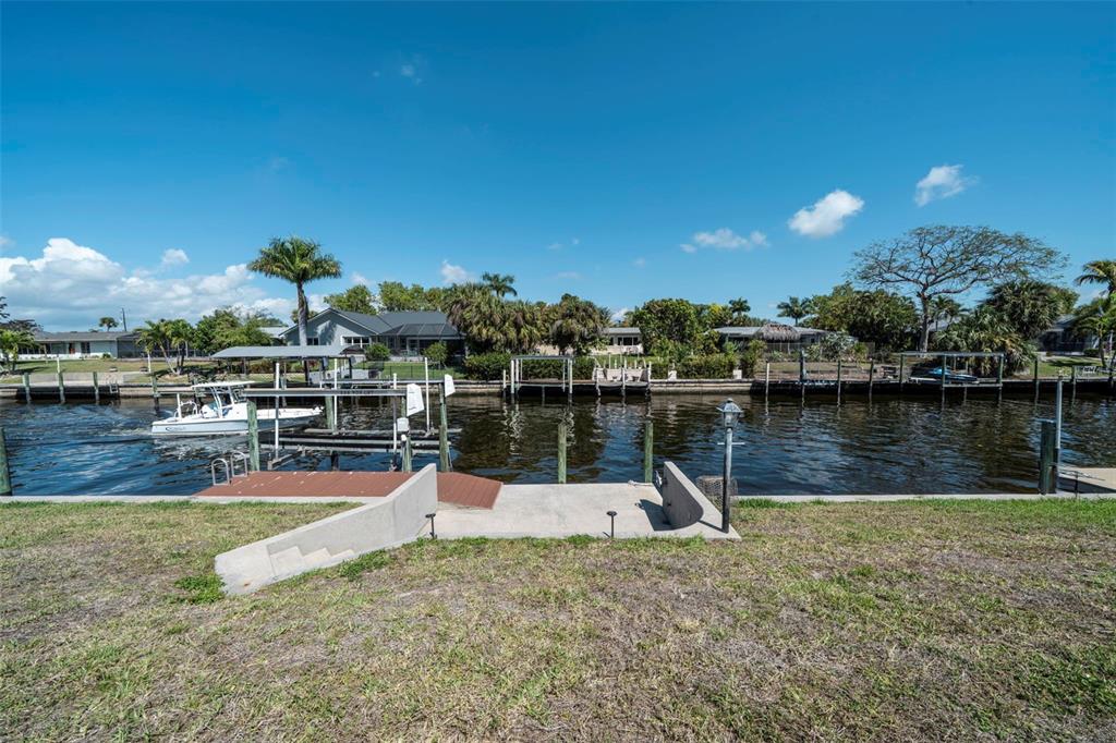 A concrete dock and boat lift sit along a canal with houses in the background — 1433 SE 28TH TERRACE, CAPE CORAL, FL