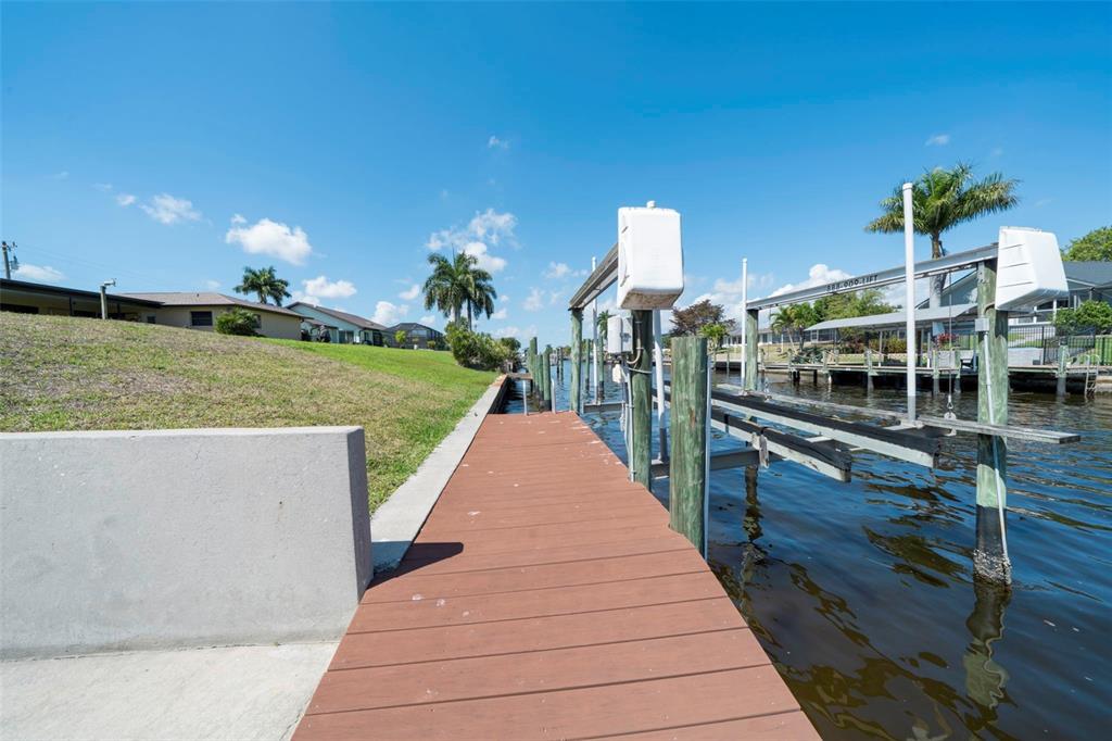 A wooden dock extends along a canal next to a grassy lawn and boat lift — 1433 SE 28TH TERRACE, CAPE CORAL, FL
