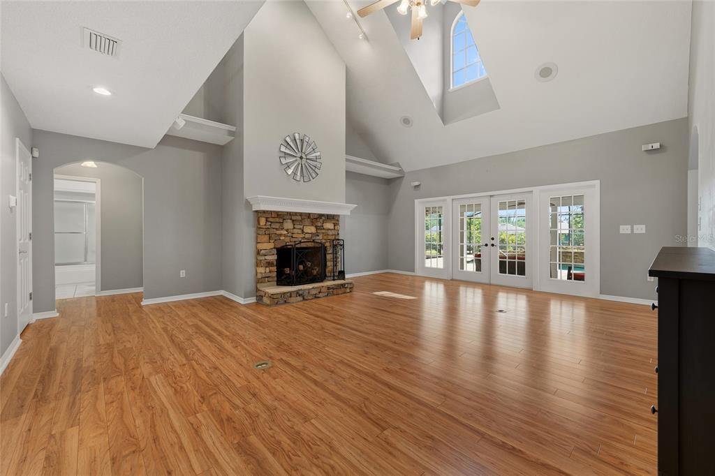 A living room with wood-look flooring, a stone fireplace, vaulted ceilings, and glass patio doors — 29314 W OLD MILL, TAVARES, FL
