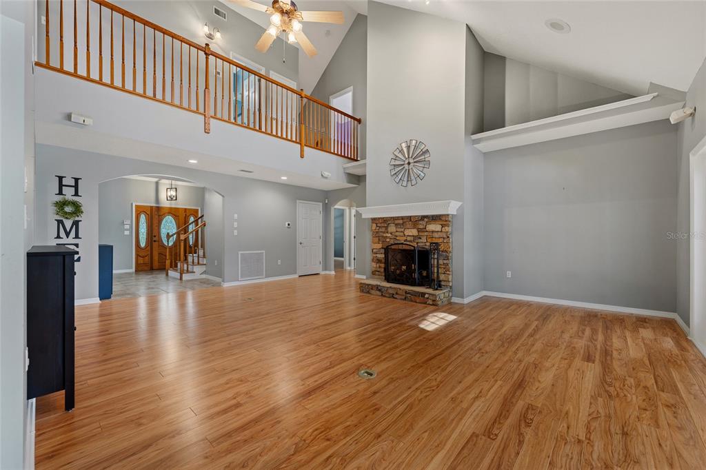 A spacious living room features wood flooring, a stone fireplace, and a second-story balcony railing — 29314 W OLD MILL, TAVARES, FL