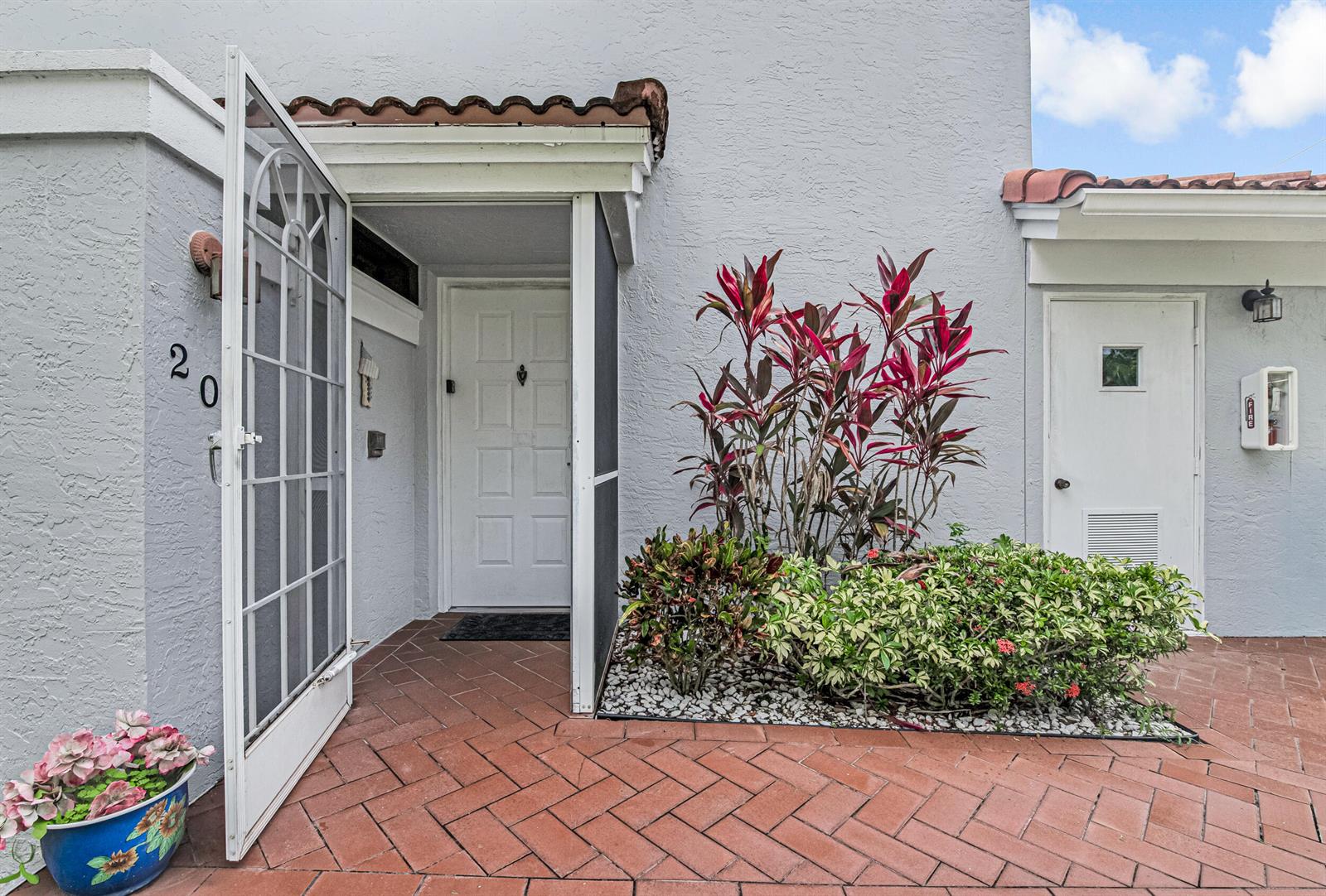 The exterior of a home features a red brick patio, a white door, and landscaping — 7384 Lake Meadow Way # 201, Boynton Beach FL 33437, BOYNTON BEACH, FL