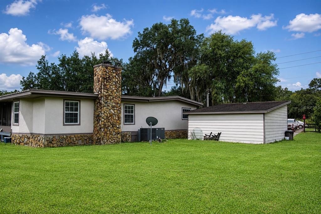 A single-story house with a stone chimney and an attached white shed in a yard — 15355 SW 85 AVENUE, DUNNELLON, FL