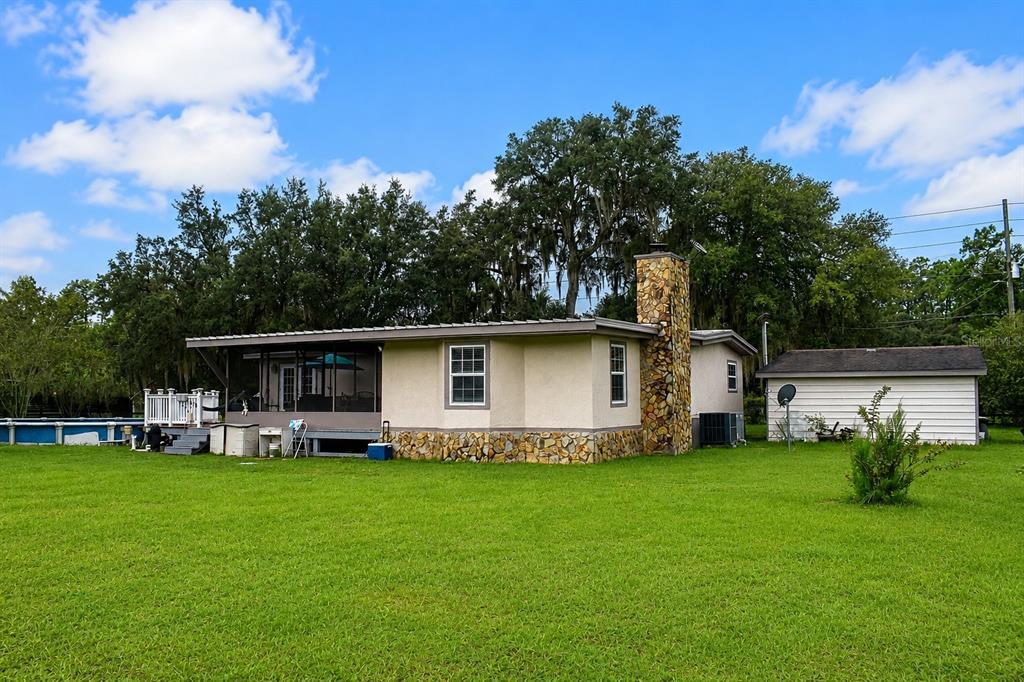 A single-story house with a stone chimney and a screened-in porch sits on a lawn — 15355 SW 85 AVENUE, DUNNELLON, FL