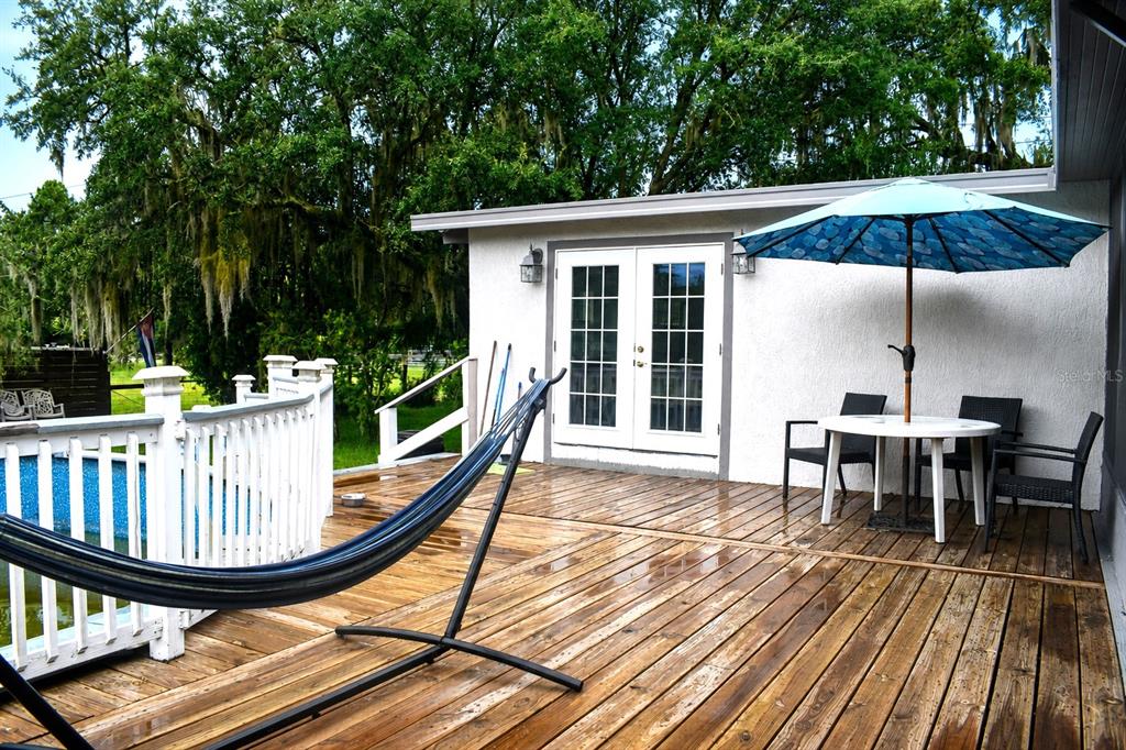 A wooden deck features a hammock, a patio table with an umbrella, and French doors — 15355 SW 85 AVENUE, DUNNELLON, FL