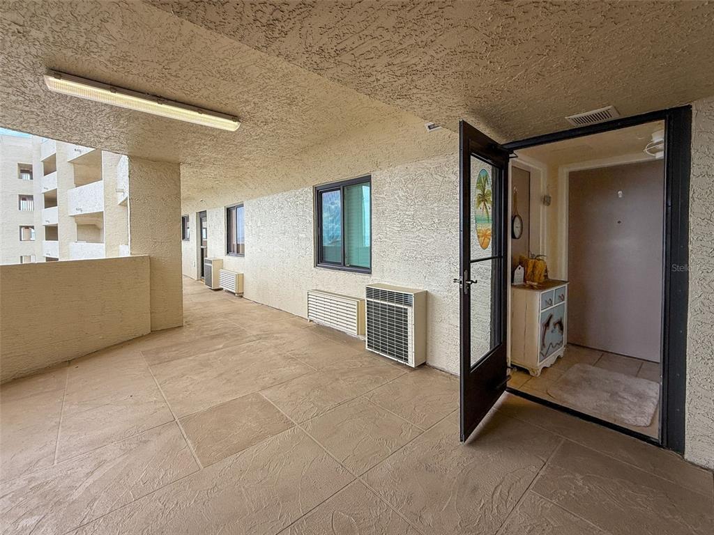 An outdoor walkway features a tiled floor, textured walls, and an open door to an interior — 6009 SEA RANCH DRIVE UNIT 608, HUDSON, FL