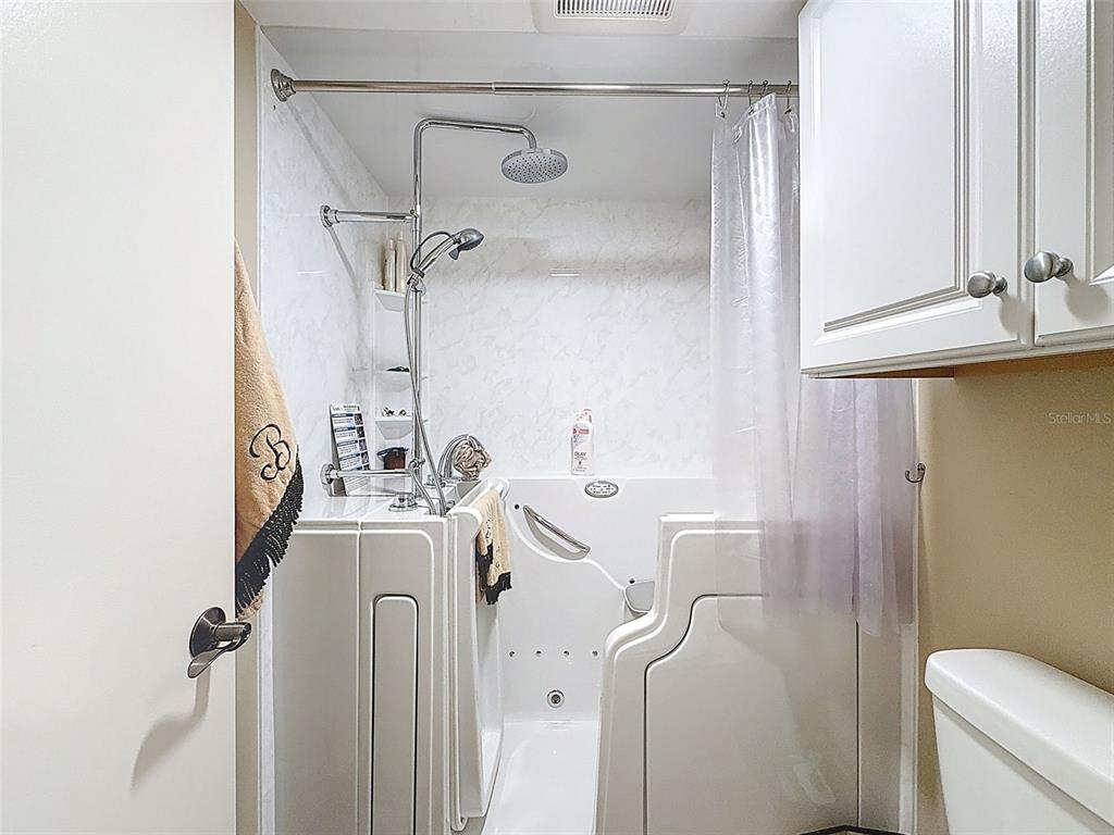 A bathroom features a white walk-in tub with a shower head and a wall-mounted cabinet — 6009 SEA RANCH DRIVE UNIT 608, HUDSON, FL