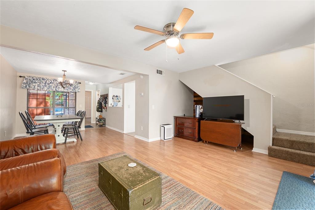 A living room with wood-look flooring, a ceiling fan, a television, and an adjacent dining area — 900 SW 62ND BOULEVARD UNIT D24, GAINESVILLE, FL
