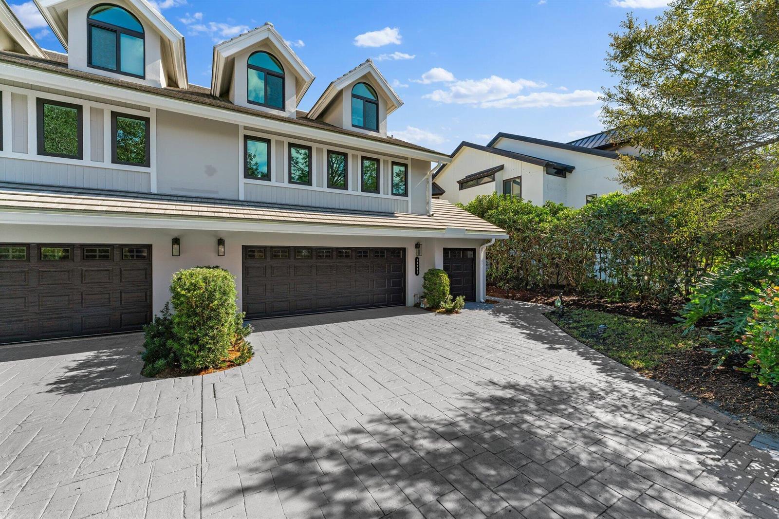 A multi-story house exterior features a gray paved driveway, three garage doors, and arched dormer windows — 18760 SE Pineneedle Lane, Jupiter FL 33469, JUPITER, FL