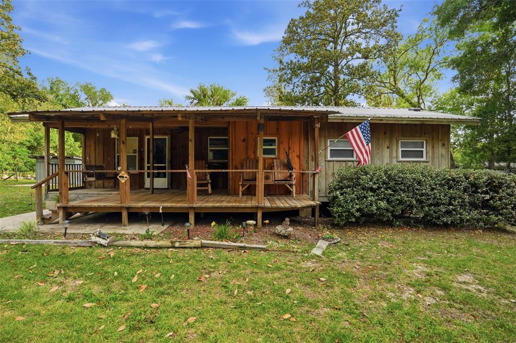 A rustic wooden cabin features a large covered front porch and an American flag — 14350 NE 191ST STREET, FORT MC COY, FL