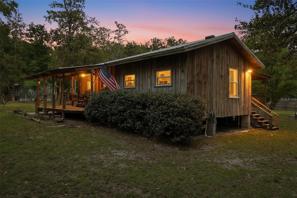 A rustic wooden cabin with a covered porch and an American flag at dusk — 14350 NE 191ST STREET, FORT MC COY, FL