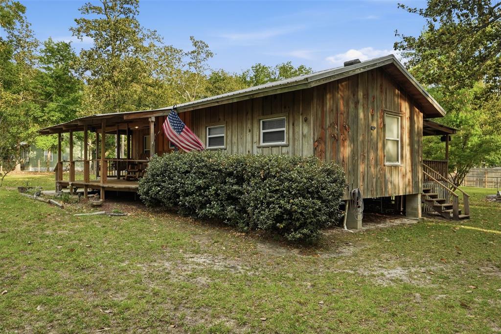 A rustic wooden cabin with a covered front porch and an American flag — 14350 NE 191ST STREET, FORT MC COY, FL