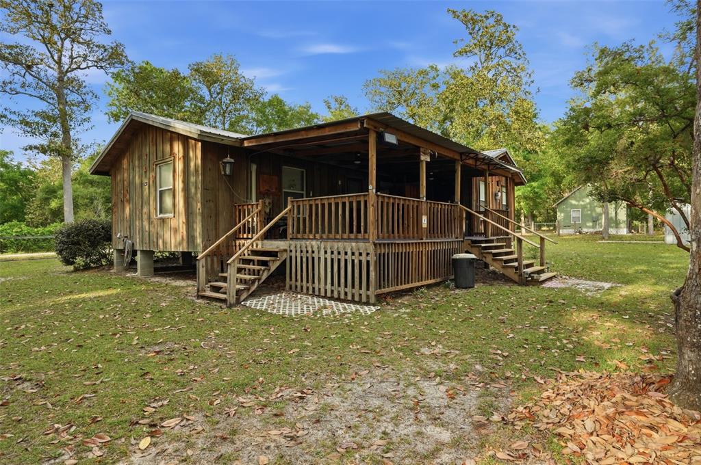 A rustic wooden cabin features a large covered porch with wooden railings and stairs — 14350 NE 191ST STREET, FORT MC COY, FL