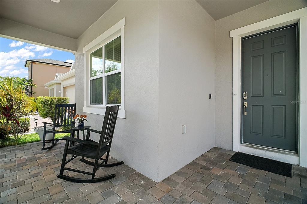 A covered front porch features a paver floor, two black rocking chairs, and a grey door — 9153 CARMELA AVENUE, DAVENPORT, FL