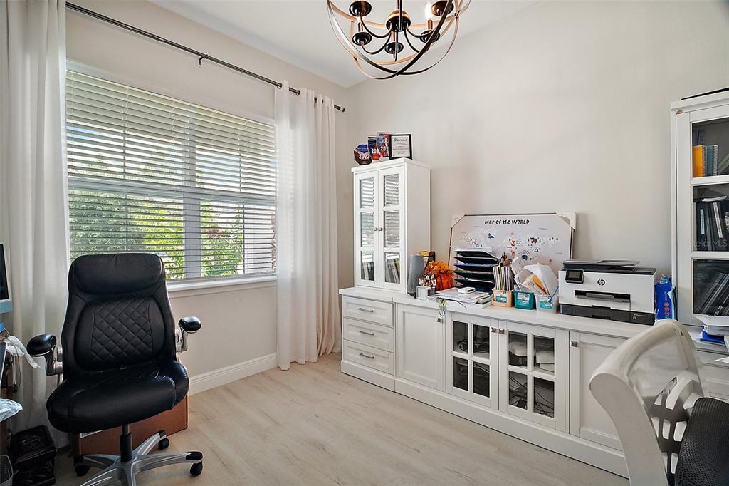 A home office features a white desk, storage cabinets, a black chair, and a window — 9153 CARMELA AVENUE, DAVENPORT, FL