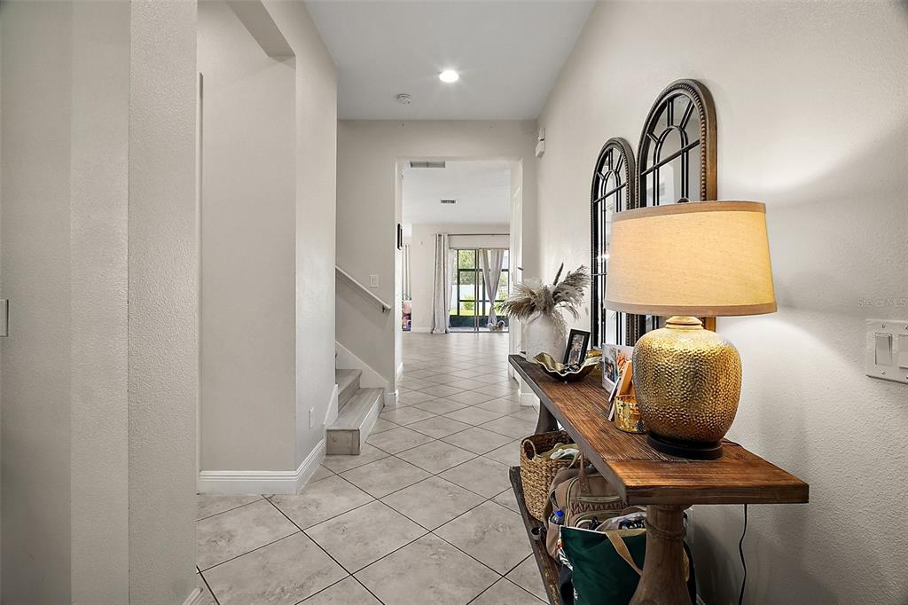 A tiled entryway features a wooden console table with a lamp and a staircase — 9153 CARMELA AVENUE, DAVENPORT, FL