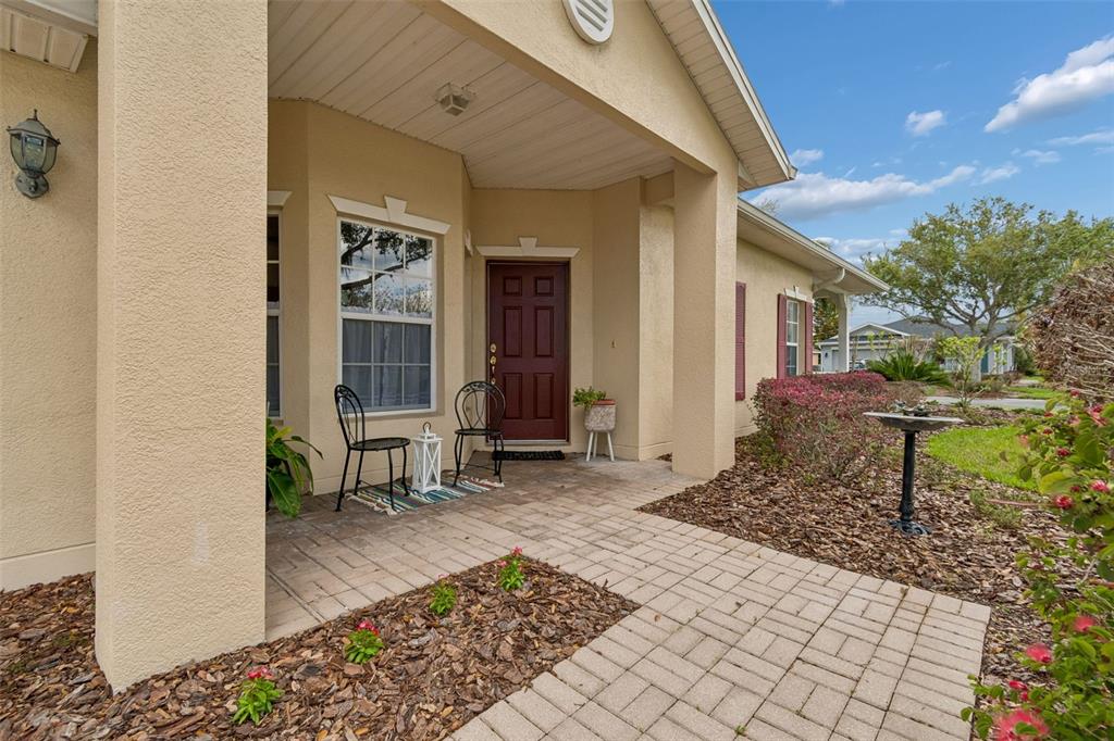 A covered entryway features a paved walkway, a dark red front door, and two chairs — 524 GLENDORA ROAD, KISSIMMEE, FL