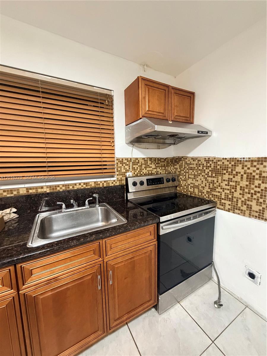 A kitchen features wood cabinets, a stainless steel stove, a sink, and a tiled backsplash — 717 NE 1st St, Hallandale Beach FL 33009, HALLANDALE BEACH, FL