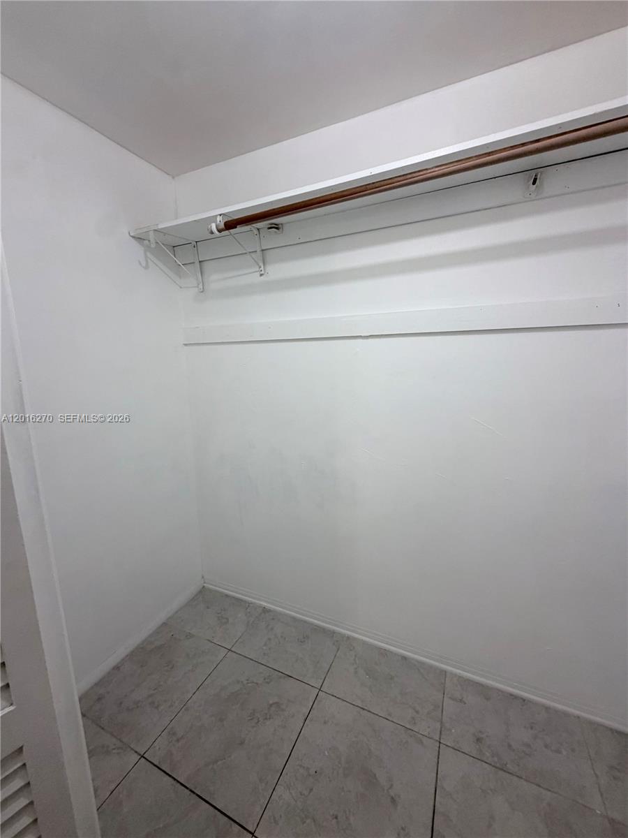 A small walk-in closet features white walls, tile flooring, and a single wooden hanging rod — 717 NE 1st St, Hallandale Beach FL 33009, HALLANDALE BEACH, FL