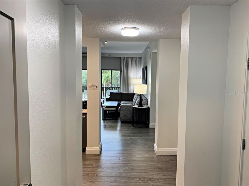 A hallway with wood-look flooring leads into a living room with a sectional sofa — 14501 GROVE RESORT AVENUE UNIT 3231, WINTER GARDEN, FL