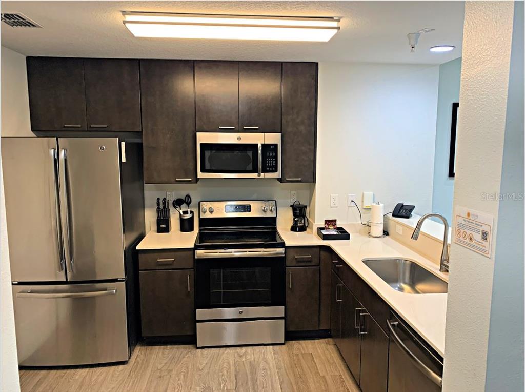 A kitchen features dark cabinets, stainless steel appliances, white countertops, and light wood-look flooring — 14501 GROVE RESORT AVENUE UNIT 3231, WINTER GARDEN, FL