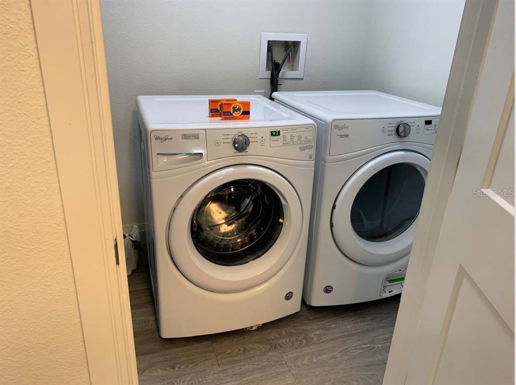 A laundry room features a white front-loading washer and dryer on a wood-look floor — 14501 GROVE RESORT AVENUE UNIT 3231, WINTER GARDEN, FL