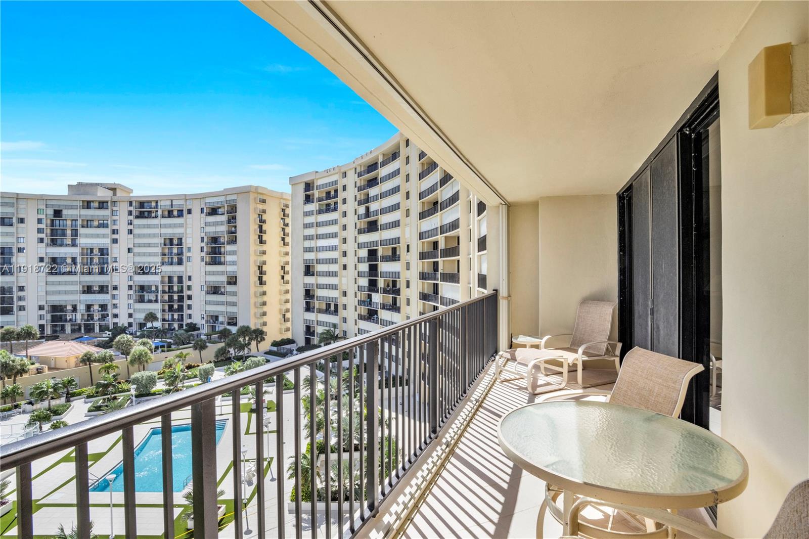 A balcony with patio furniture overlooks a swimming pool and surrounding apartment buildings — 200 Ocean Trail Way # 609, Jupiter FL 33477, JUPITER, FL