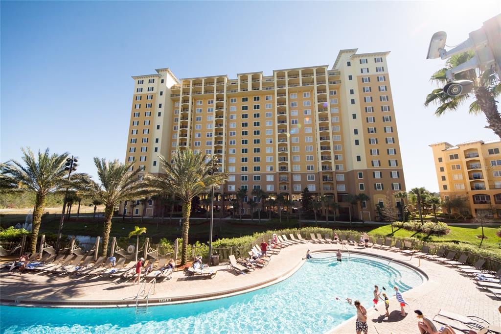 A large multi-story hotel building overlooks a swimming pool with lounge chairs and palm trees — 8112 POINCIANA BOULEVARD UNIT 1802, ORLANDO, FL