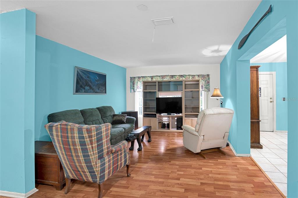 A living room features light blue walls, wood-look flooring, a sofa, a recliner, and shelving — 104 LUDWIG AVENUE, CRESCENT CITY, FL
