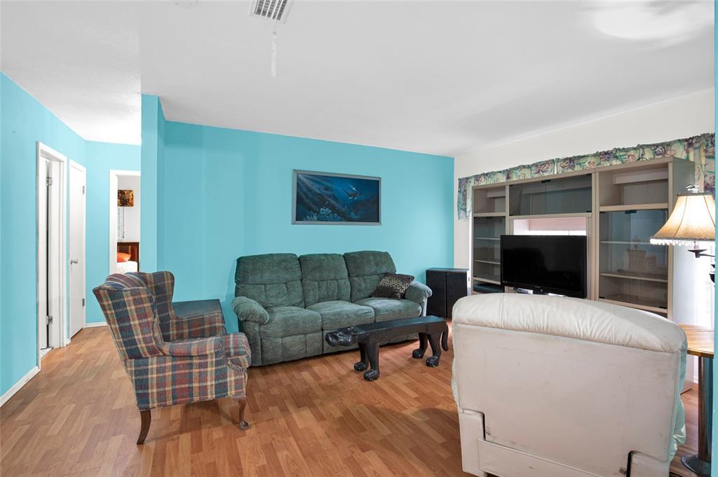 A living room with turquoise walls, wood-look flooring, a green sofa, and a plaid armchair — 104 LUDWIG AVENUE, CRESCENT CITY, FL