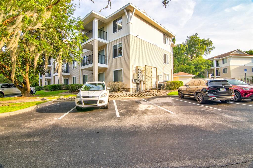 A three-story apartment building with beige siding and a parking lot in the foreground — 3921 SW 34TH STREET UNIT 216, GAINESVILLE, FL