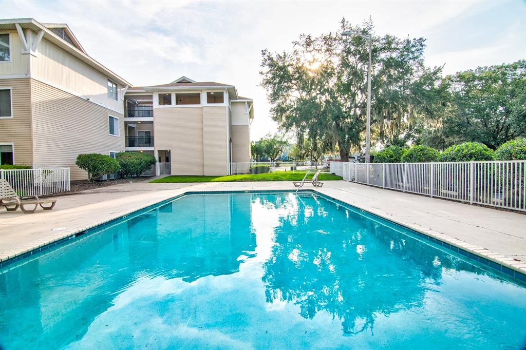 A rectangular swimming pool sits in front of a multi-story apartment building with beige siding — 3921 SW 34TH STREET UNIT 216, GAINESVILLE, FL