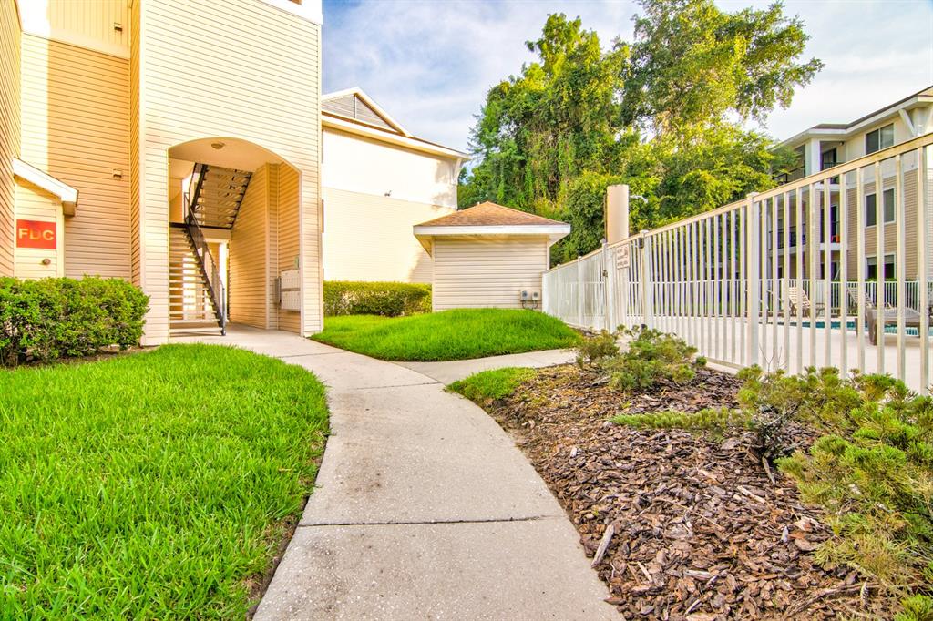 A concrete walkway leads past a tan apartment building toward a fenced pool area — 3921 SW 34TH STREET UNIT 216, GAINESVILLE, FL