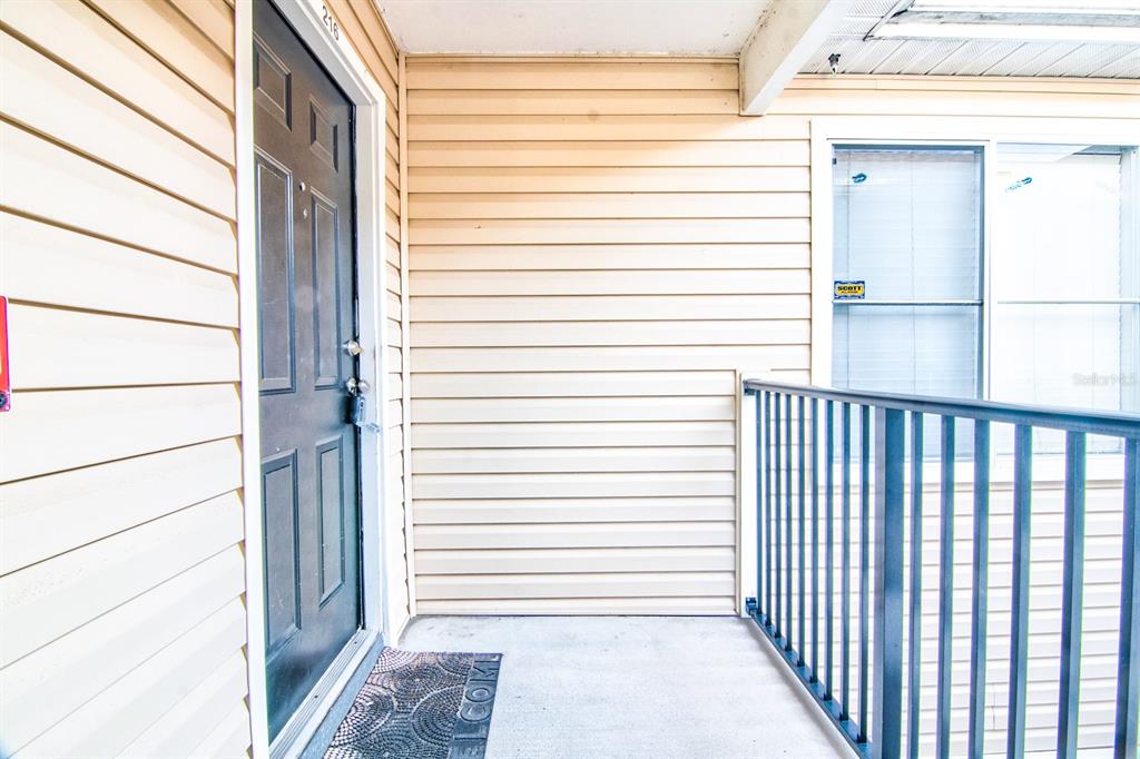 A covered porch features beige horizontal siding, a black front door, and a metal railing — 3921 SW 34TH STREET UNIT 216, GAINESVILLE, FL