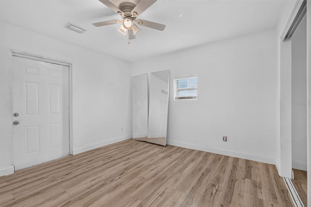A bedroom with white walls, wood-look flooring, a ceiling fan, and two leaning floor mirrors — 2005 SCHULTE AVENUE, DAYTONA BEACH, FL