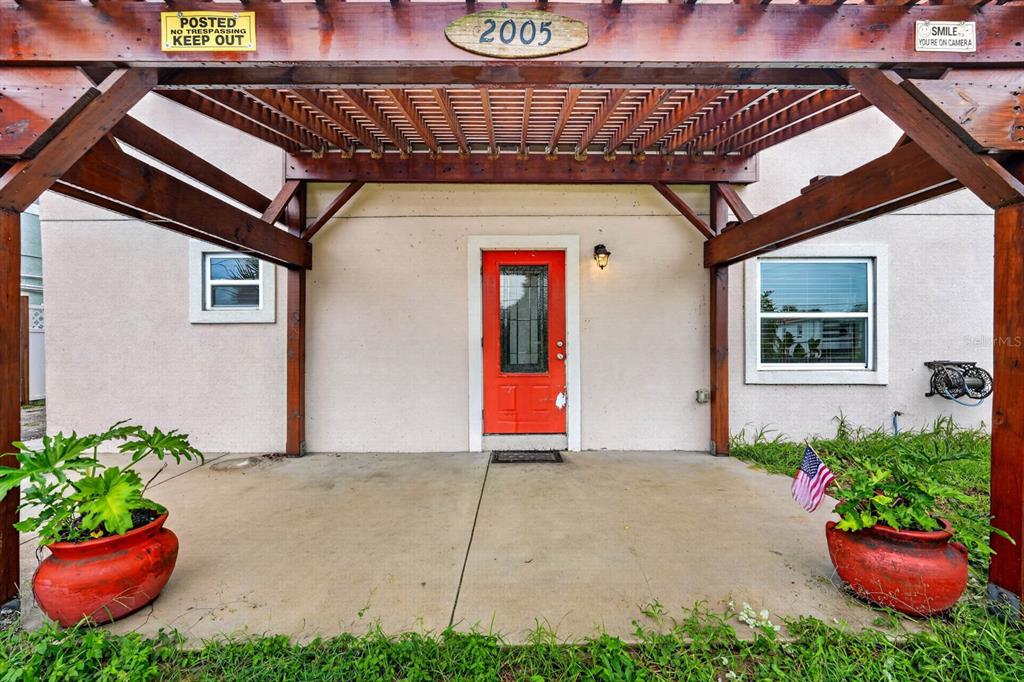 A red front door sits under a wooden pergola on a concrete porch — 2005 SCHULTE AVENUE, DAYTONA BEACH, FL