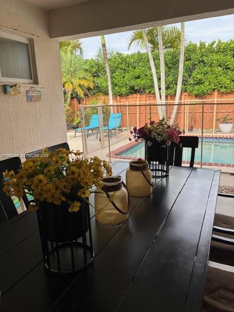 A patio dining table with flower arrangements overlooks a backyard pool and fenced lawn — 15751 SW 141st Ct, Miami FL 33177, MIAMI, FL