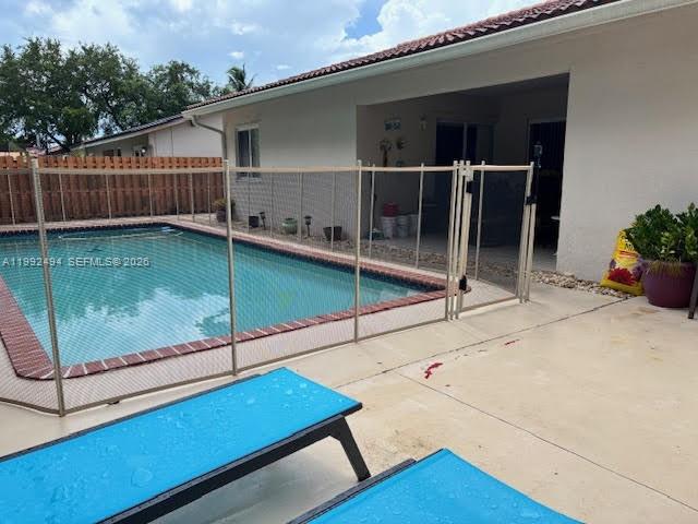 A swimming pool with a safety fence sits on a patio next to a house — 15751 SW 141st Ct, Miami FL 33177, MIAMI, FL
