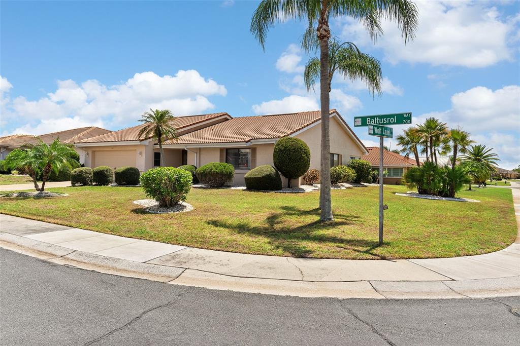 A single-story house with a tiled roof and manicured landscaping sits on a corner lot — 701 BALTUSROL WAY, SUN CITY CENTER, FL
