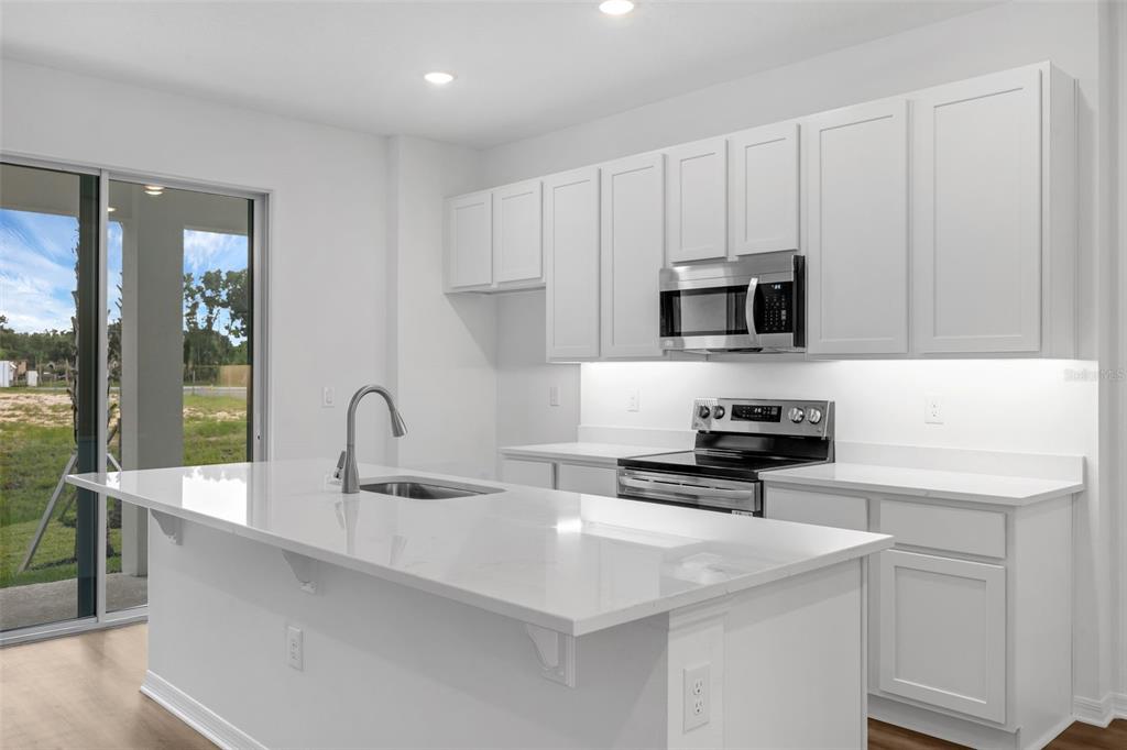 A modern kitchen features white cabinets, quartz countertops, a center island, and stainless steel appliances — 1156 CYPRESS ELM DRIVE, DELAND, FL